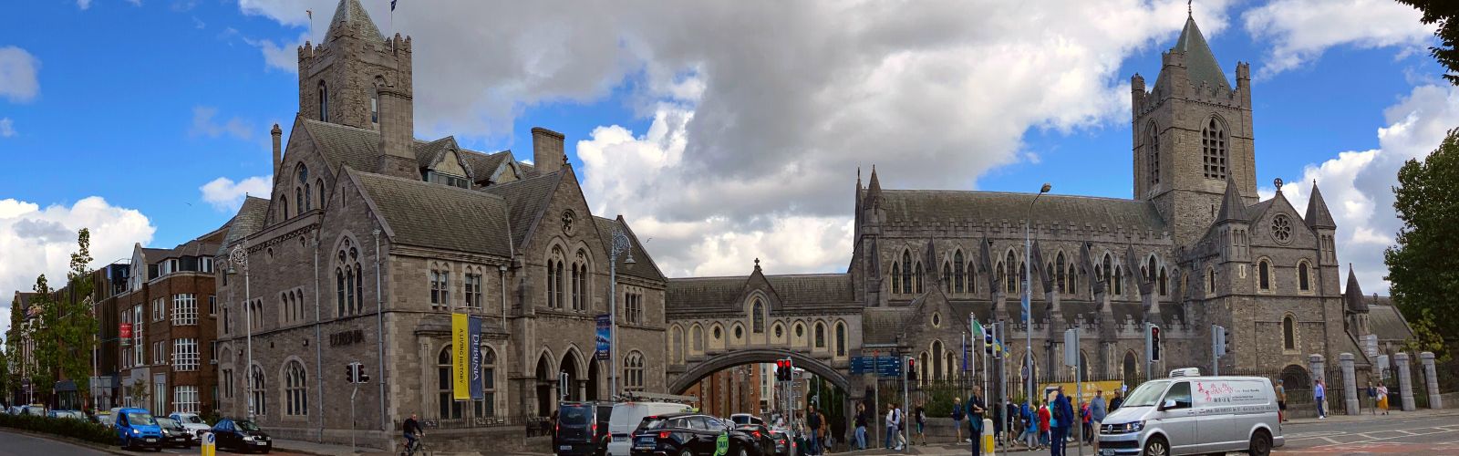 A stone castle with several peaked roofs has a bridge allowing cars to pass underneath it. 